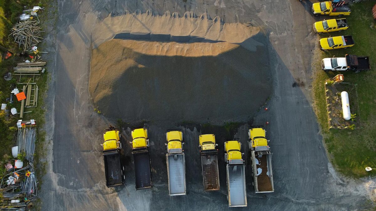 Drone aerial view of yellow trucks aligned by a gravel heap at an industrial earthwork site